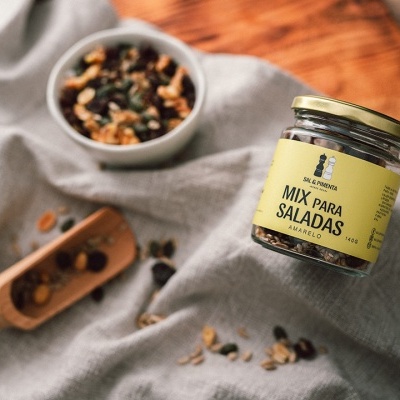 Frasco de mix para saladas, colher de madeira e prato com nozes sobre tecido cinzento