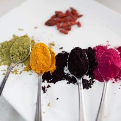 Colheres com pós coloridos verde, amarelo, roxo e rosa sobre fundo branco