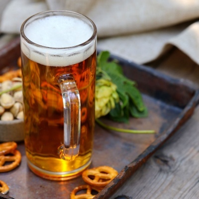 Caneca de cerveja com espuma numa bandeja com pretzels e pistácios