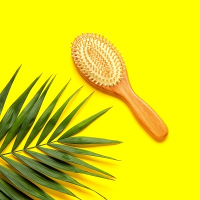 Escova de cabelo de madeira clara com cerdas claras sobre fundo amarelo e folha verde