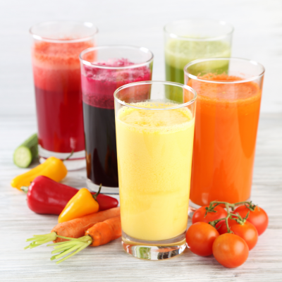Cinco copos de sumos naturais coloridos com cenoura, pimento, pepino e tomate.