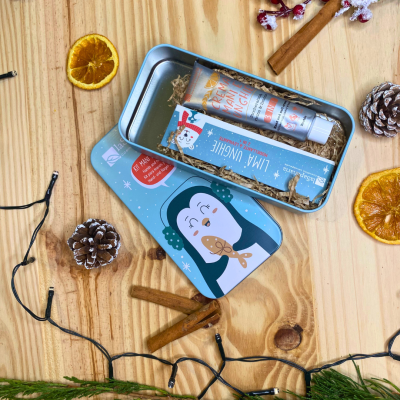 Conjunto de creme para mãos com embalagem metálica ilustrada e decoração natalina sobre mesa de madeira