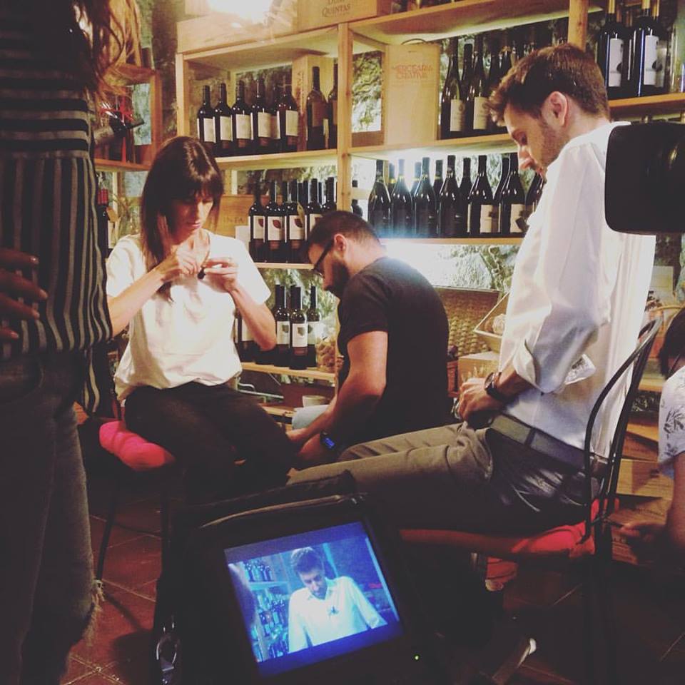 Três pessoas sentadas em frente a prateleiras de garrafas de vinho num espaço interior.