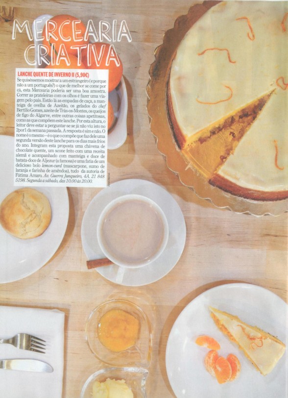Mesa com bolo branco decorado, fatia servida, chávena, pão e talheres.
