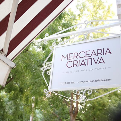 Placa comercial metálica branca com texto roxo, tecto listrado vermelho e branco e árvores verdes