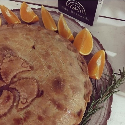 Tarte com massa dourada decorada, gomos de laranja e ervas num prato de madeira