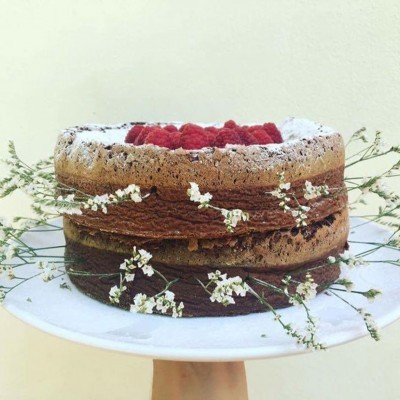 bolo de chocolate com framboesas e flores brancas num prato branco