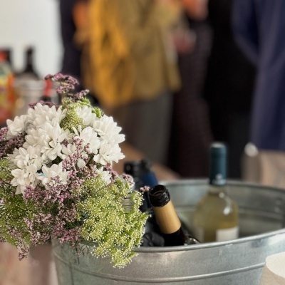 Balde metálico com garrafas e arranjo floral com flores brancas e detalhes roxos e verdes