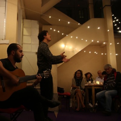 Grupo de pessoas com iluminação decorativa num ambiente interior com homem a tocar guitarra e outro a cantar