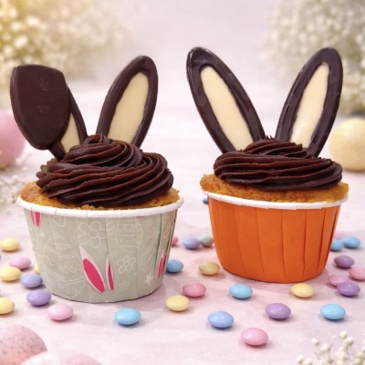 Dois cupcakes decorados com creme de chocolate e orelhas de chocolate em embalagem cinza e laranja, com confeitos coloridos à volta