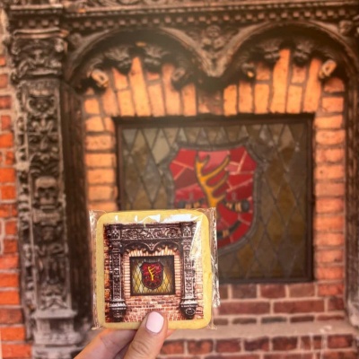 Bolacha com imagem de moldura e vitral segurada perante parede de tijolos com janela e vitral similar