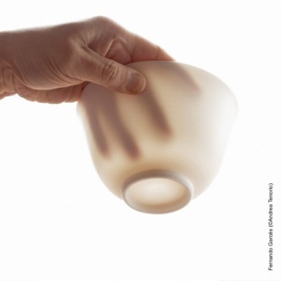 Taça translucida fosca em vidro branco segura por mão contra luz