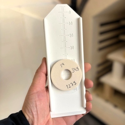 Ferramenta plástica branca com marcações graduadas e peça circular bege com escrita manuscrita.