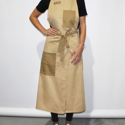 Avental comprido bege com bolsos marrons usado por pessoa em fundo branco