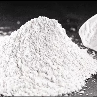 Montanha de pó branco fino em superfície preta com colher branca ao fundo.