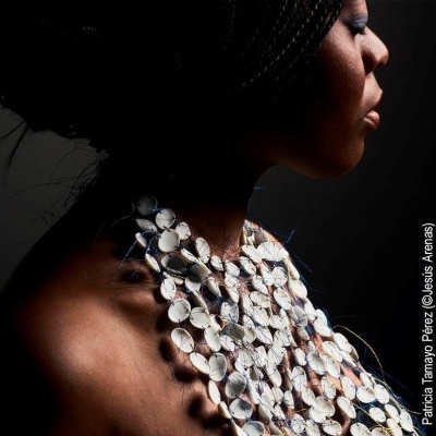 Colar branco grande e artístico no pescoço de mulher negra com fundo escuro