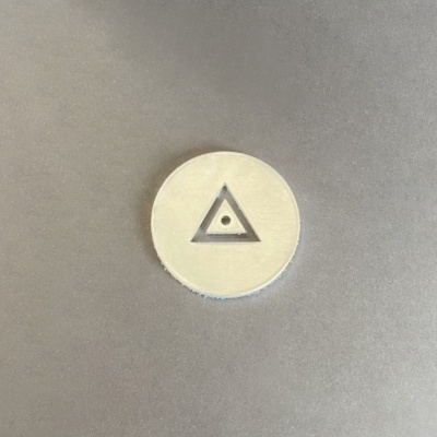 Objeto redondo bege com símbolo triangular recortado no centro numa superfície cinza