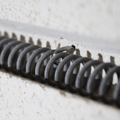 Mola metálica preta com fio solto numa superfície branca rugosa
