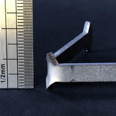 Peça metálica prateada ao lado de régua metálica sobre fundo escuro