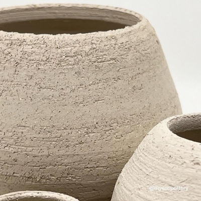 Três vasos cerâmicos em tons bege com textura rugosa sobre fundo branco