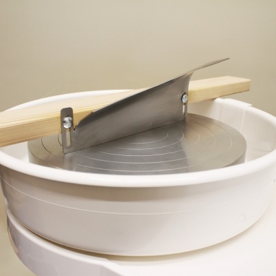 Roda de oleiro branca com prato metálico e lâmina de corte.