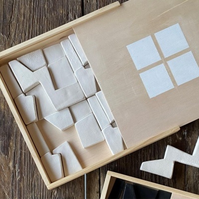 Peças geométricas brancas em caixa de madeira clara com tampa com quatro quadrados brancos.