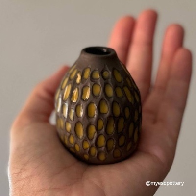 Pequeno vaso de cerâmica com manchas amarelas na palma da mão