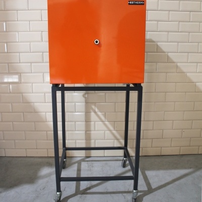 Armário metálico laranja em estrutura preta com rodas contra parede de azulejos brancos