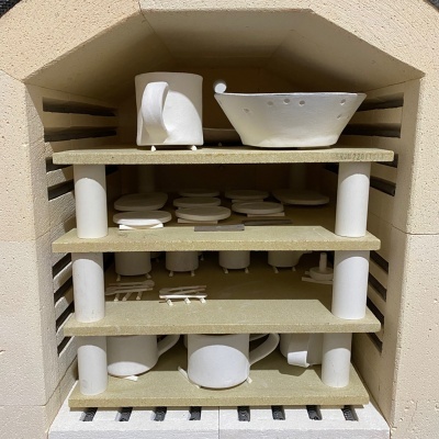 Peças de cerâmica branca empilhadas em prateleiras dentro de um forno.