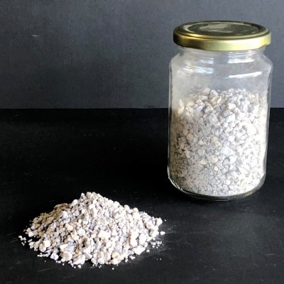 Frasco de vidro com tampa dourada e cacos brancos e bege em superfície preta