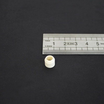 Pequena peça branca cilíndrica junto a uma régua metálica sobre fundo escuro