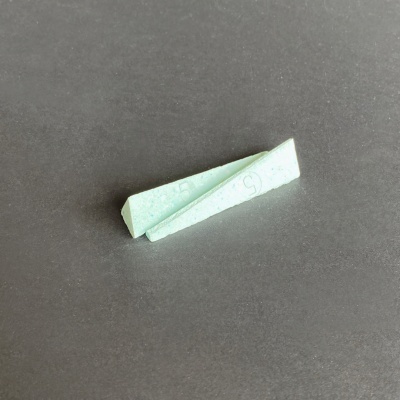 Avião de papel verde claro com marcas sobre superfície cinza