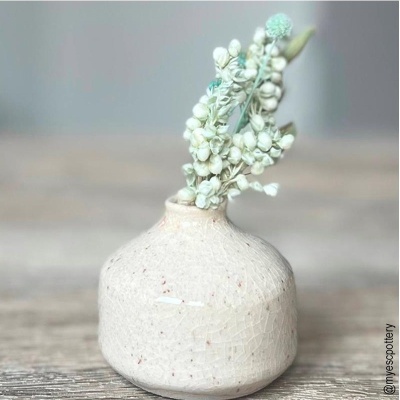 Vaso cerâmico branco com flores artificiais sobre mesa de madeira