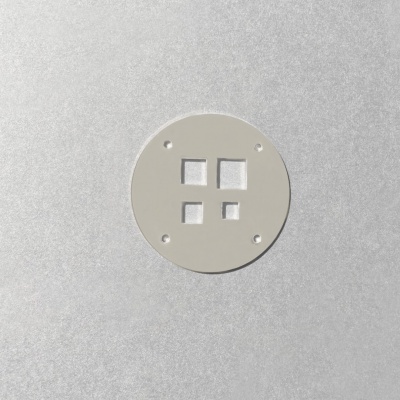 Placa redonda cinza claro com quatro aberturas quadradas numa superfície metálica prateada