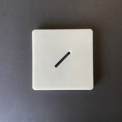 Painel elétrico quadrado branco com fenda no centro sobre superfície escura