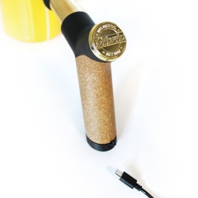 Bastão com pega em cortiça e tampa dourada com texto 'Fluorita' e cabo USB preto sobre fundo branco