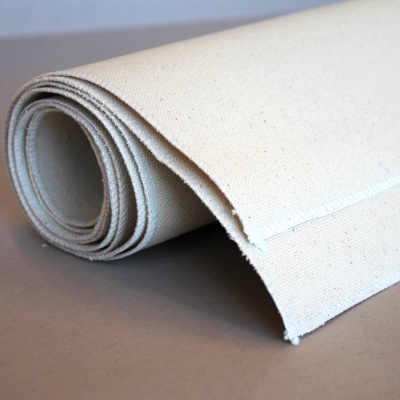 Rolo de tecido cru com textura visível sobre superfície cinzenta