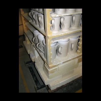 Canecas de cerâmica branca não pintadas em prateleiras dentro de um forno