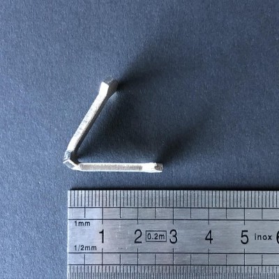 Objeto metálico branco angular ao lado de régua métrica sobre fundo azul