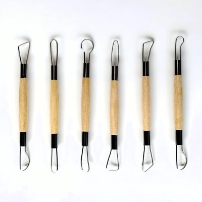 Seis ferramentas de escultura com cabos de madeira e pontas metálicas variadas sobre fundo branco
