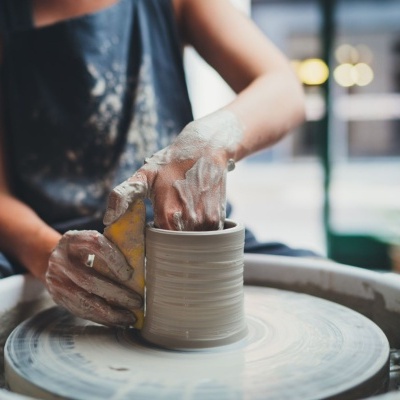 Pessoa a moldar cerâmica em roda de oleiro com mãos sujas de barro