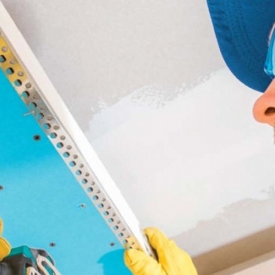 Pessoa a usar furadeira elétrica azul para fixar placa branca num teto azul