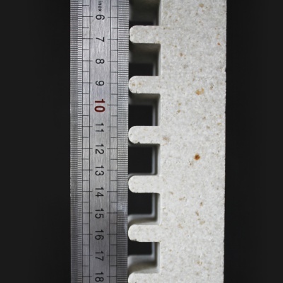 Régua metálica junto a peça branca granulada com recortes em dentes