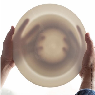 Mãos segurando um prato transparente translúcido bege iluminado de trás