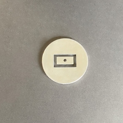 Disco redondo creme com retângulo e ponto no centro sobre superfície cinzenta