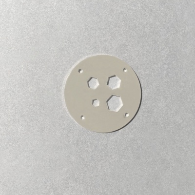 Placa redonda de metal cinza com recortes hexagonais e furos pequenos