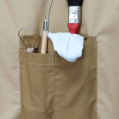 Bolsa de tecido castanho claro com pincel, pinça e pano branco nos bolsos