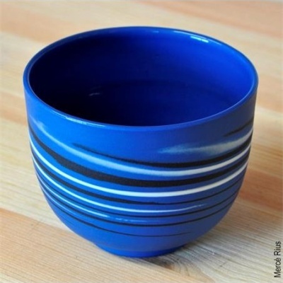 Vaso ou tigela azul com faixas pretas e brancas numa mesa de madeira clara.