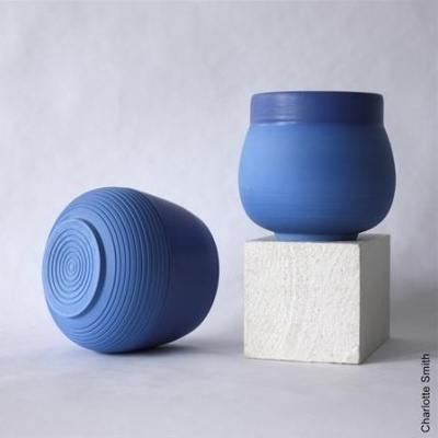 Dois vasos cerâmicos azuis, um sobre cubo branco, outro deitado, fundo cinza