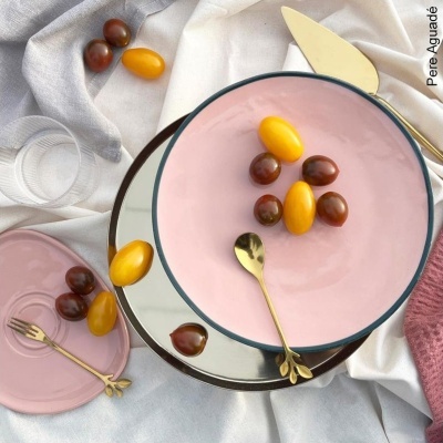 Conjunto de pratos rosa e espelhado com talheres dourados e tomates cherry em fundo de tecidos